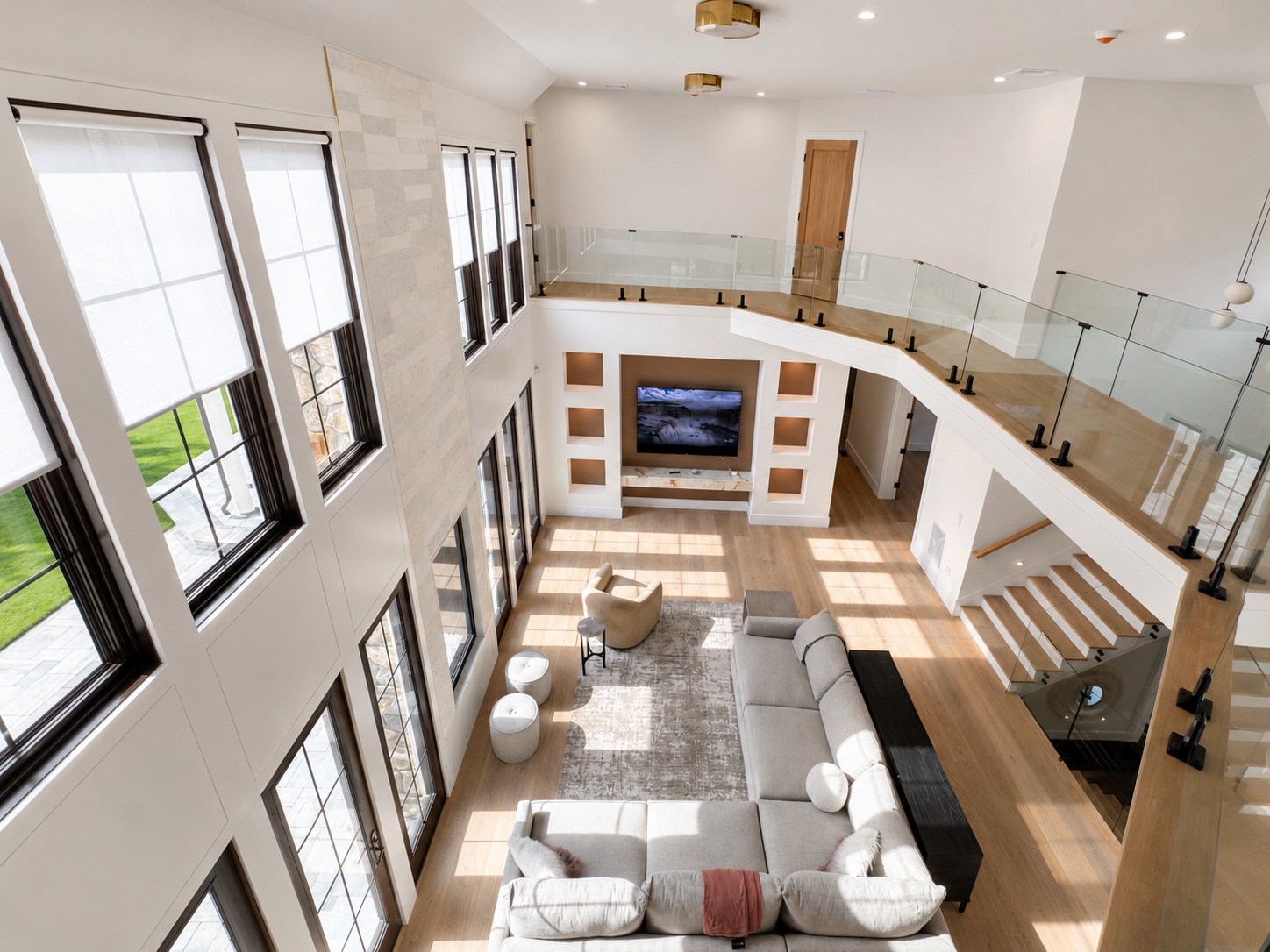 High ceiling living room painting with white walls, black trim, glass railing, and natural wood floors