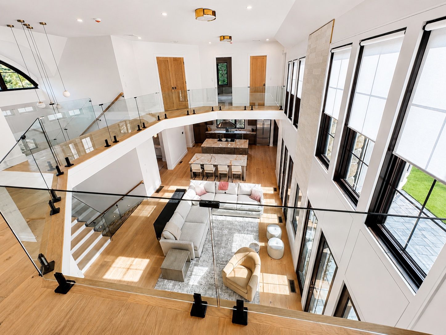 Open concept living room painting with tall white walls, dark window trim, glass railing, and wood floors